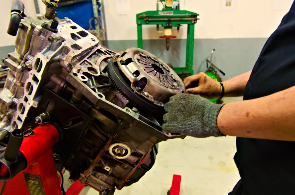A mechanic reassembly a car engine while holding a clutch