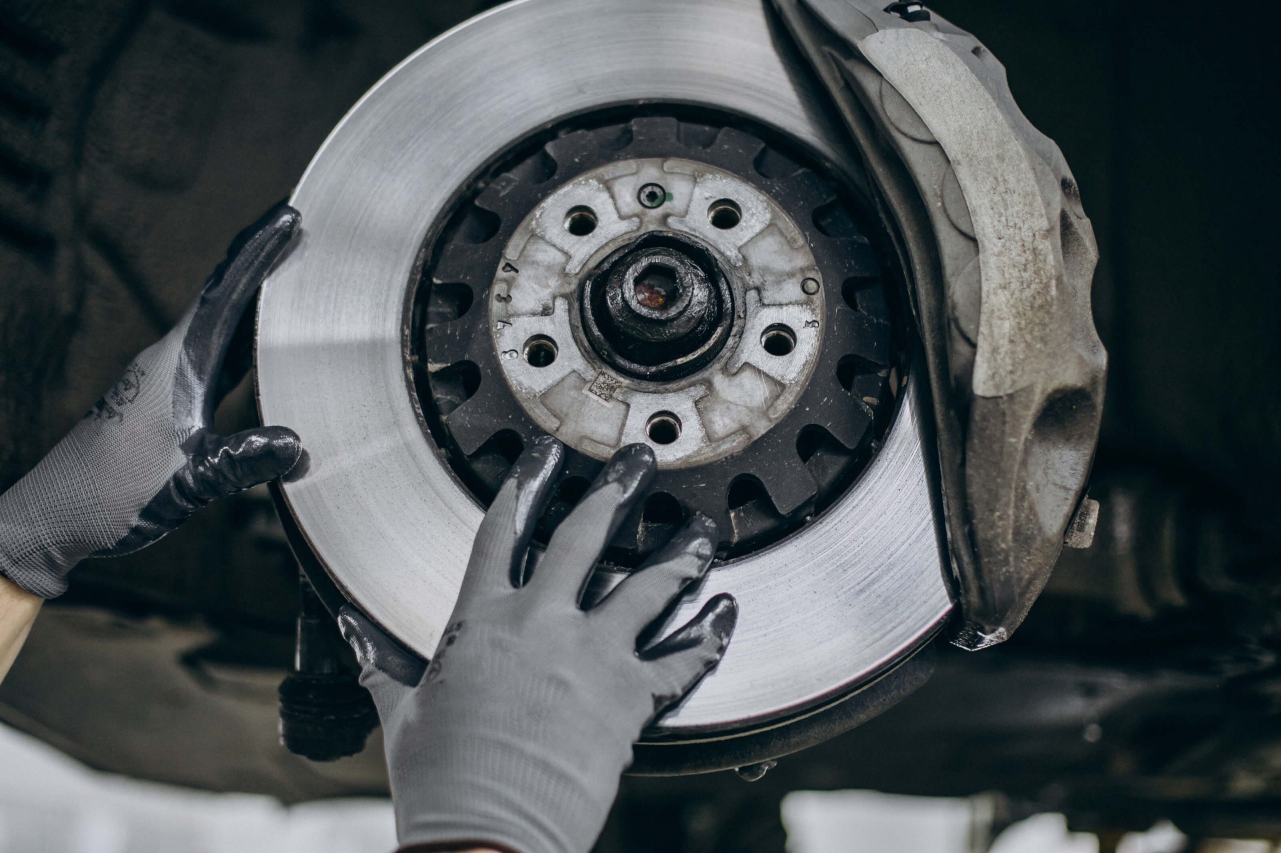 Gloved brake specialist installing a rotor into a brake calliper under a suspended car