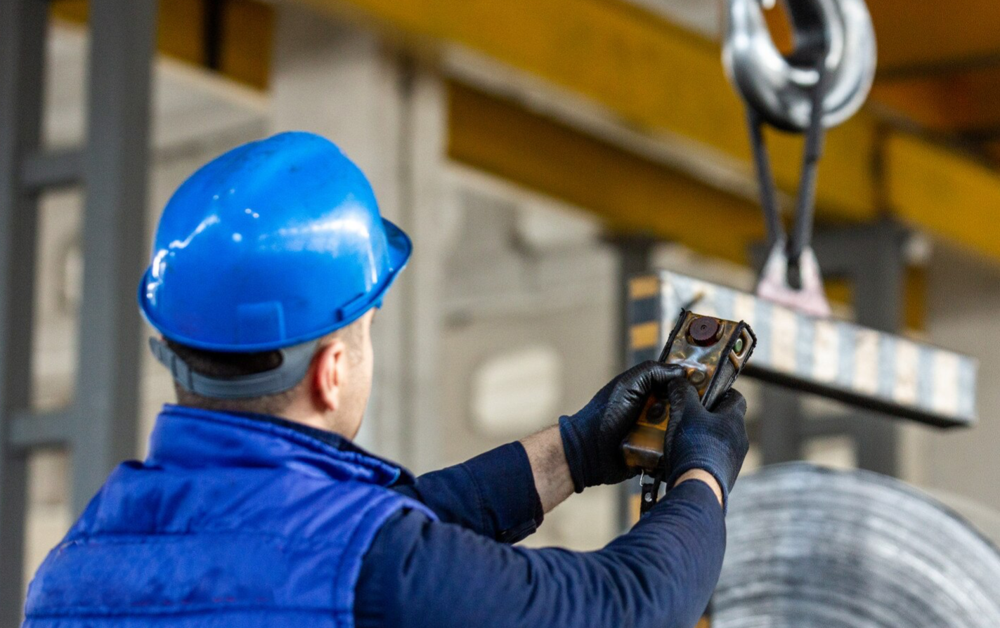 Worker operating crane brake controls in a factory.