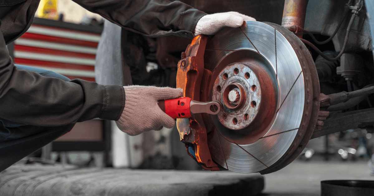 Gloved mechanic fitting brake system parts to a stripped down, elevated car