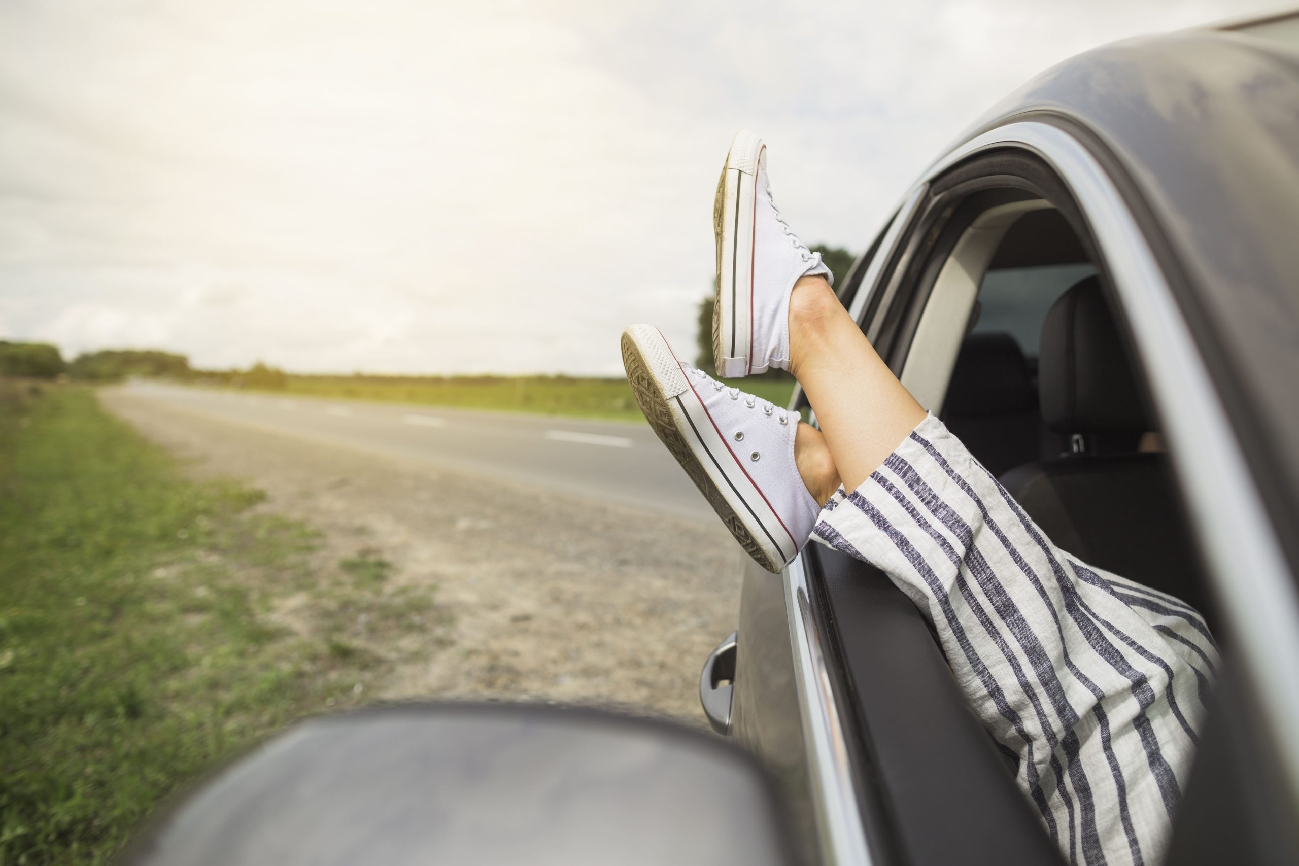 A young lady’s legs dangling her legs out of the window of a car with one of the best braking systems