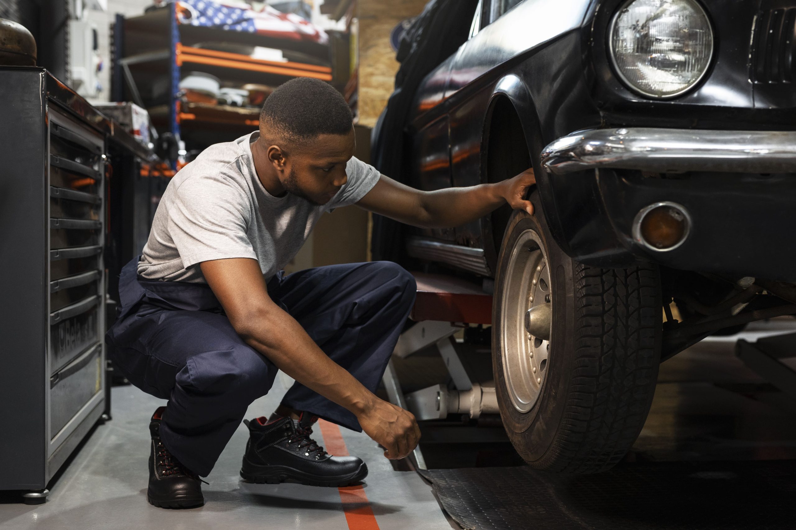 An African mechanic looking under the wheel of a vintage car to calculate the brake replacement cost